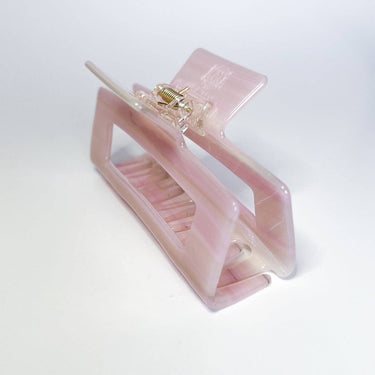 A translucent, pale pink hair claw clip with a visible metal spring is angled on a white background.